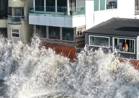 A large Pacific Ocean wave crashes over a seawall against Long Beach coastal homes
